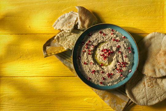 Baba ganoush or mutabal, Middle Eastern eggplant dip sauce garnished with pomegranate seeds with a rustic napkin and pita bread
