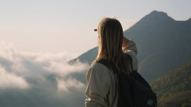 woman backpacker is standing on top of mount and admiring nature