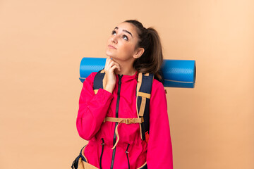 Young mountaineer girl with a big backpacker isolated on beige background thinking an idea