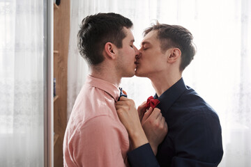 Gay couple kissing and keeping hands at the each other bowties