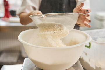 Woman hands sifting flour with flour filter while preparing dough at the table