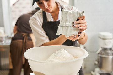 Woman putting ingredients at the tank while preparing dough at the table