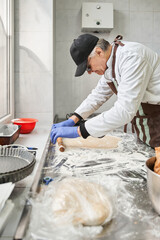 Baker man kneading dough on table with flour and rolling pin