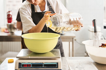 Woman putting oil at the tank and weighs it while preparing dough at the table