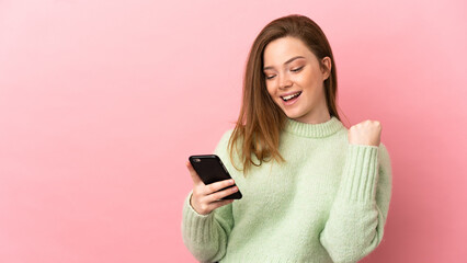 Teenager girl over isolated pink background with phone in victory position