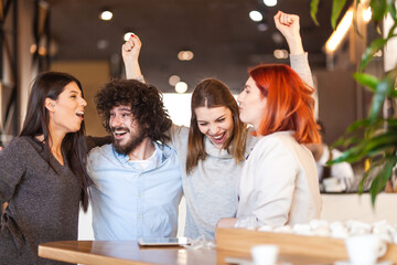 Four friends at a cafe having fun and cheering. Successful young people