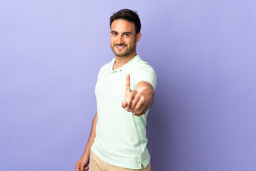 Young handsome man isolated on purple background showing and lifting a finger