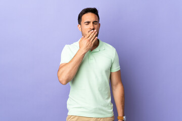 Fototapeta premium Young handsome man isolated on purple background yawning and covering wide open mouth with hand