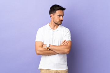 Young handsome man isolated on purple background keeping the arms crossed