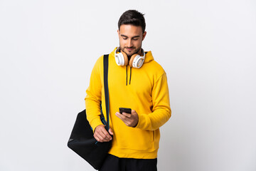 Young sport man with sport bag isolated on white background sending a message with the mobile
