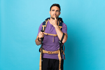 Young caucasian man with backpack and trekking poles isolated on blue background having doubts while looking up