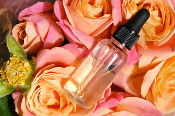 Facial serum bottle or essential oil on floral background. Transparent cosmetics container. Beauty product packaging mockup. Organic cosmetics concept. Top view.