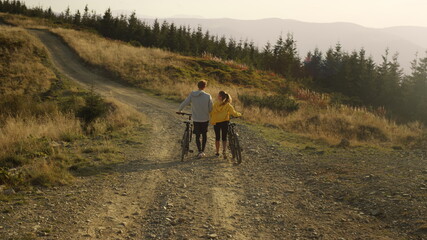 Fototapeta na wymiar Guy and girl having walk with bicycles. Bicyclists looking around landscape