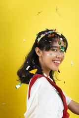 Beautiful young woman throwing confetti and looking happy on yellow background