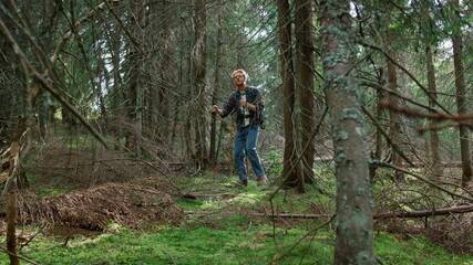 Man walking with trekking poles in green forest. Handsome guy trekking in woods