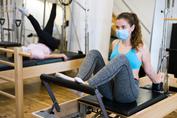 Gym woman protective mask pilates stretching sport in reformer bed