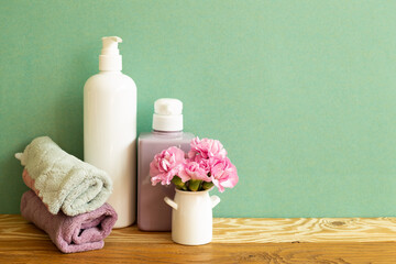 Fototapeta na wymiar Soap bottles and towel with flowers on wooden shelf. Bathroom skin care and spa concept