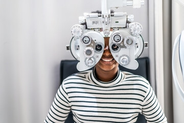 Smiling young woman african american afro hair doing Eye test on optical phoropter, checking on her...