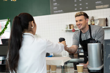 Barista cafe or bartender serving coffee to customer at coffee shop with happy and smile. Female customer receiving coffee from barista hands in coffee shop. Small business and purchase concept