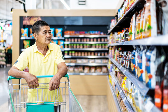 Asian senior man shopping trolley choosing other products in supermarket
