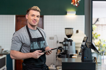 Barista cafe wearing apron and using digital tablet at coffee shop with happy and smiling. Small business owner concept