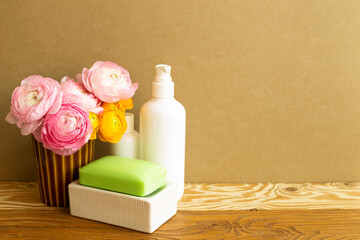 White bottles and soap with flowers on wooden shelf. Bathroom skin care and spa concept