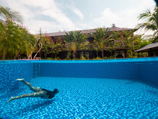 A woman in the bottom of the pool and view of tropical villa with green trees.
