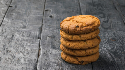 A stack of homemade cookies with chocolate chips on a black wooden table.