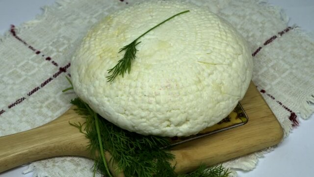 Round soft white homemade cheese. Adyghe cheese with greens lying on wooden board. 4K