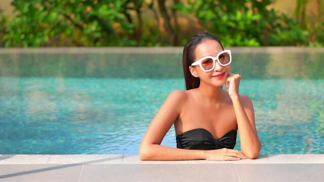 Close up of an attractive young woman leaning her chin on her hand as she enjoys the pool at a resort. Title space
