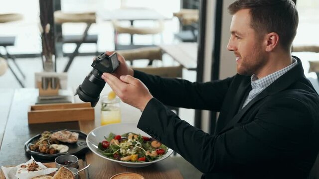 Stylish young man takes pictures on a mirrorless camera dishes at the table