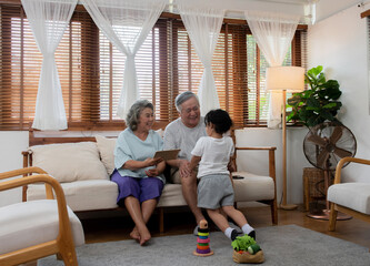 Obraz na płótnie Canvas Happy Asian family spending time together at home. Grandfather and grandmother play with little grandchild girl in living room. Retirement senior couple having fun with cute baby granddaughter.
