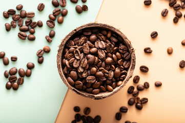black arabica coffee beans, aromatic in a coconut dish, sprinkled beans on the table, light background, close-up, top view