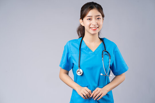 Image of young Asian female doctor wearing blue uniform on grey background
