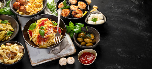 Assortment of Italian pasta with traditional sauces for dinner on dark background.