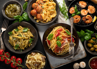 Assortment of Italian pasta with traditional sauces for dinner on dark background.