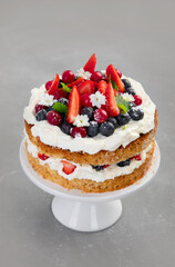 Delicious homemade cake with fresh berries and mascarpone cream on gray background.