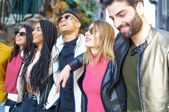 A group of young people of different races, millennial generation, walk hugging together with their arms on their shoulders expressing a concept of diversity, friendship and unity.