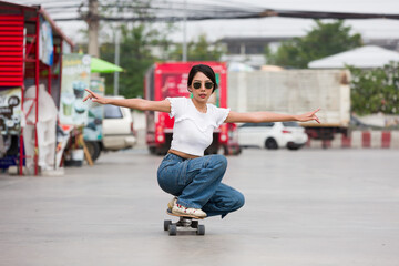 Asian young woman skater riding on skateboard on courtyard at gas station with wear sunglasses....