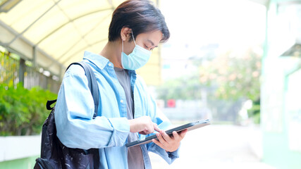 Young asian university student holding digital tablet while wearing protection mask at campus, social distancing, covid 19