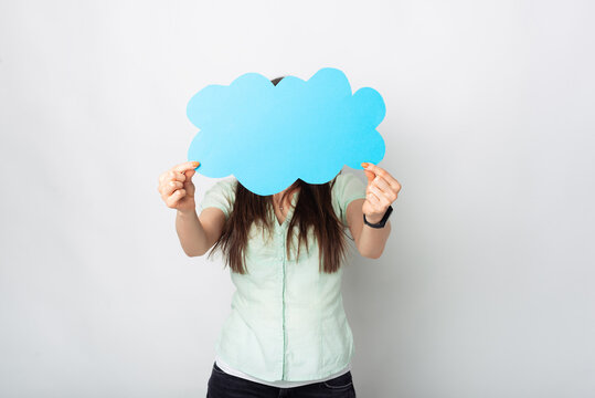 A photo of a woman holding with both hands in front of her a cloud shaped paper with free space in it near a white wall