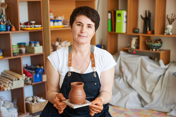 woman potter in a black apron holds a piece of red clay in her hands