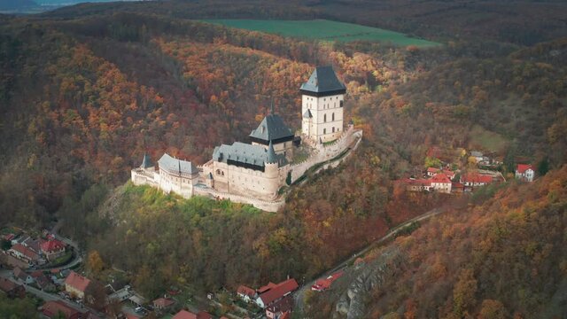 Aerial view of the famous Karlstein Castle - a beautiful medieval castle standing on the hill, overlooking the dense forest. Houses of the small village scattered at the foothills.