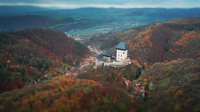 Aerial view of the famous Karlstein Castle - a beautiful medieval castle standing on the hill, overlooking the dense forest. Villages are scattered through the valley below. A tilt-shift video.