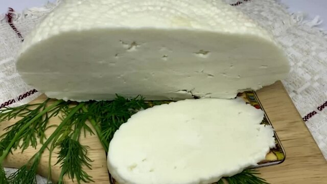 Round soft white homemade sliced cheese. Adyghe cheese with greens lying on wooden board. HD