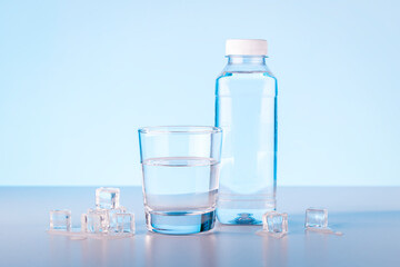 Bottle and glass of natural water with ice cubes.