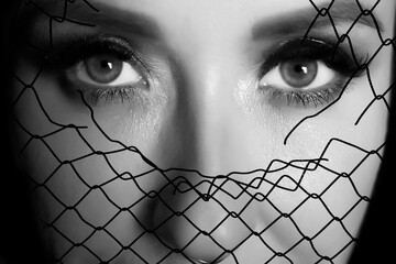 Portrait of a charming young female looking at camera serious  behind metal mesh. close up image.
