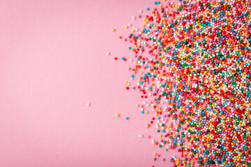 Colored sprinkles on pink background.