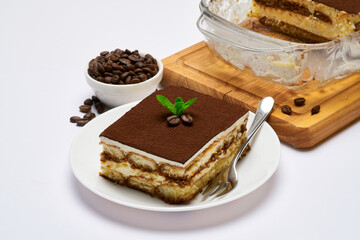Traditional Italian Tiramisu dessert in glass baking dish and portion on plate on white background