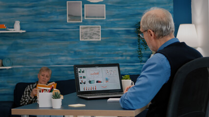 Middle aged senior older man e-learning online concept, watching business graphs, charts on laptop computer remote working, social distance learning, writing noteson notebook from home office.